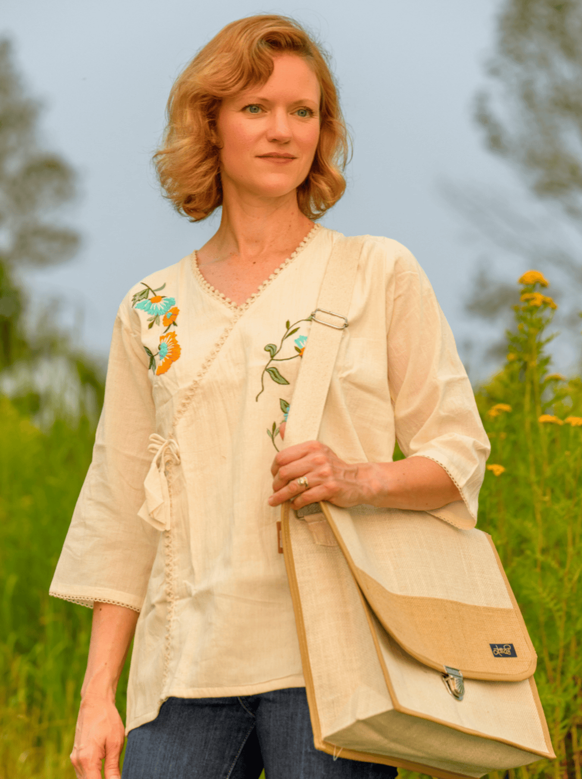 Woman holding a beige bag with floral embroidery in a natural setting